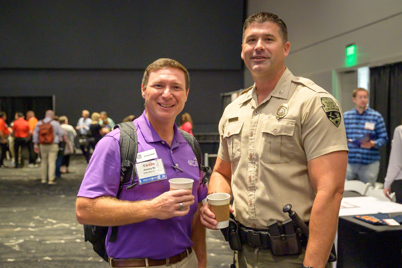 Wildlife Conservation game warden smiling and holding coffee with an attendee.