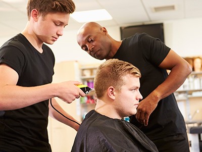 Teacher Helping Male Students Training To Become Hairdressers