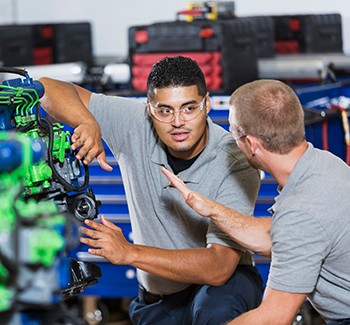 Two multi-ethnic young men in vocational school, taking a class on reparing diesel engines.  They are working on an engine that has had parts painted different colors for training purposes.  They are wearing safety glasses.