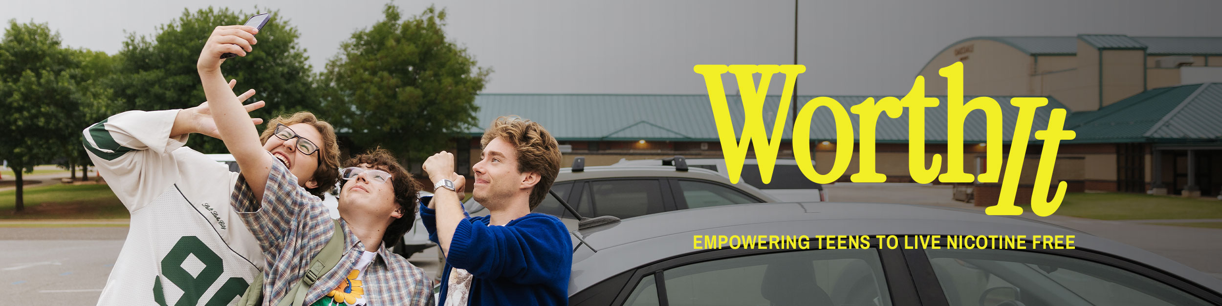 Three teens taking a selfie together in a school parking lot, smiling and laughing, next to the "Worth It" logo and tagline "Empowering Teens to Live Nicotine Free."