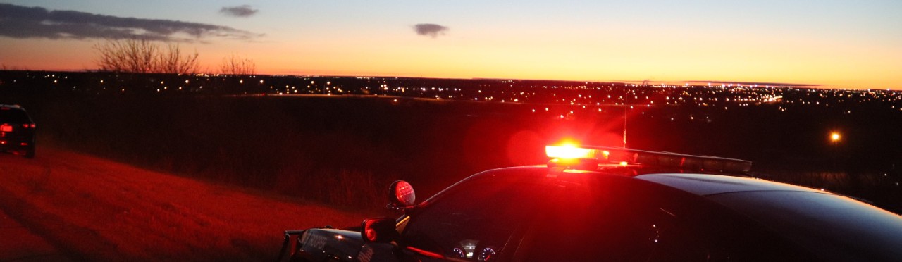 police cruiser with red lights on top of vehicle and a sunrise in the background.