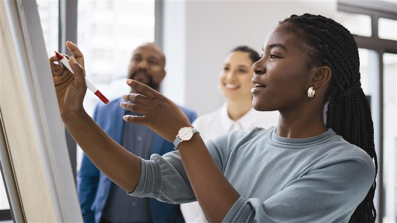 Woman writing on a flip chart during a meeting while two colleagues watch.