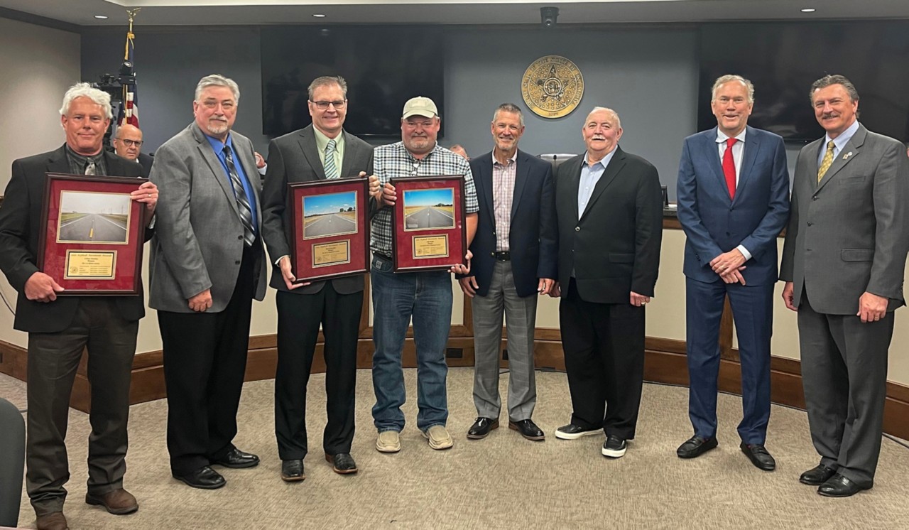 Group of men, three holding awards for quality construction with other transportation officials