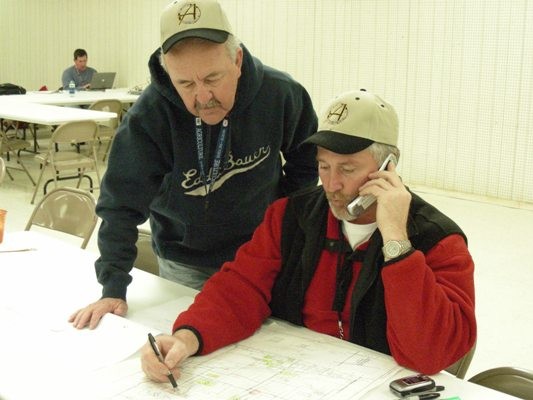 Two men looking a map with one man on a cell phone. 