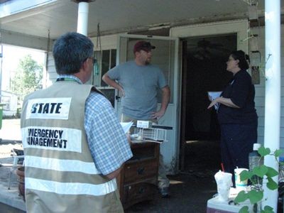 Emergency Management workers talk with woman on her porch. 