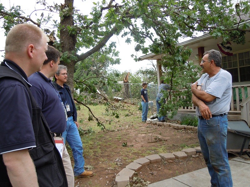 Three men talking to man about a storm damage of a building. 