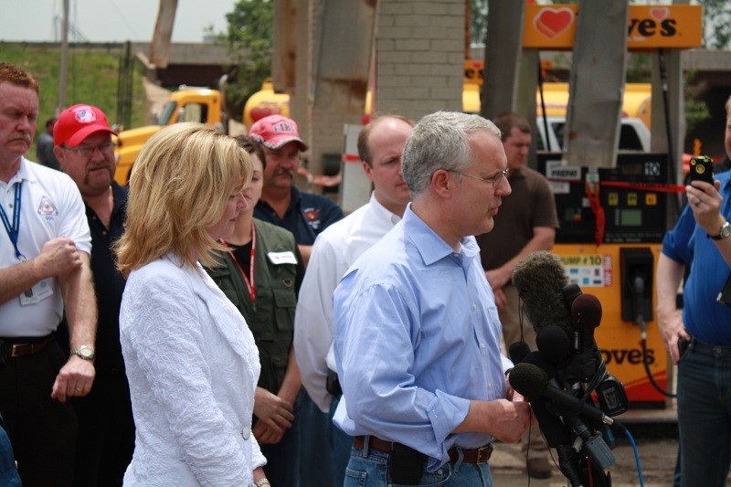 Gov. Brad Henry talks with the media in front of a microphone with many people behind him. 