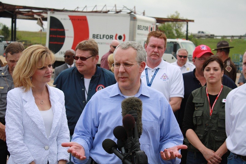 Gov. Brad Henry talks with the media in front of a microphone with many people behind him. 