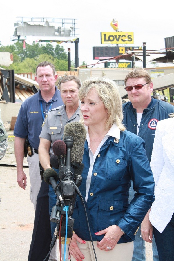 Lt. Gov. Mary Fallen in front of media microphones with police and emergency management workers behind her.