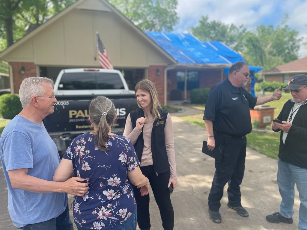 OEM staff talking with a couple in their drive way. Their home has tarps on the roof. 
