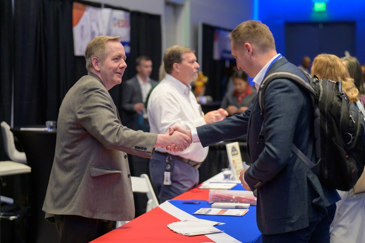 State staff shaking hands with a 2024 attendee at the Military and Veterans Affairs booth.