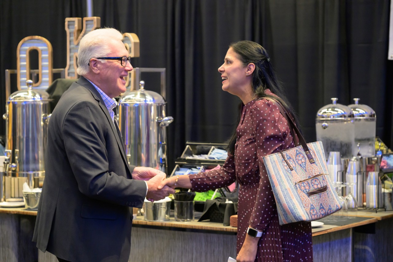 Two attendees shake hands in front of the refreshments table