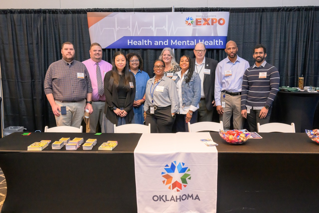 A group of 10 state staff members smile while standing at the Health and Mental Health booth