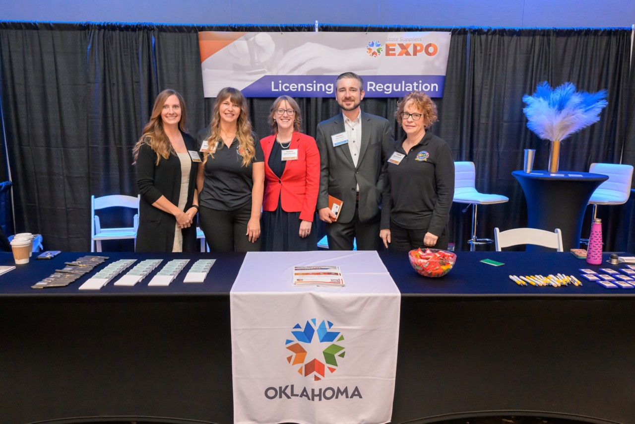 Four state staff members and an attendee smiling at the Licensing and Regulation booth