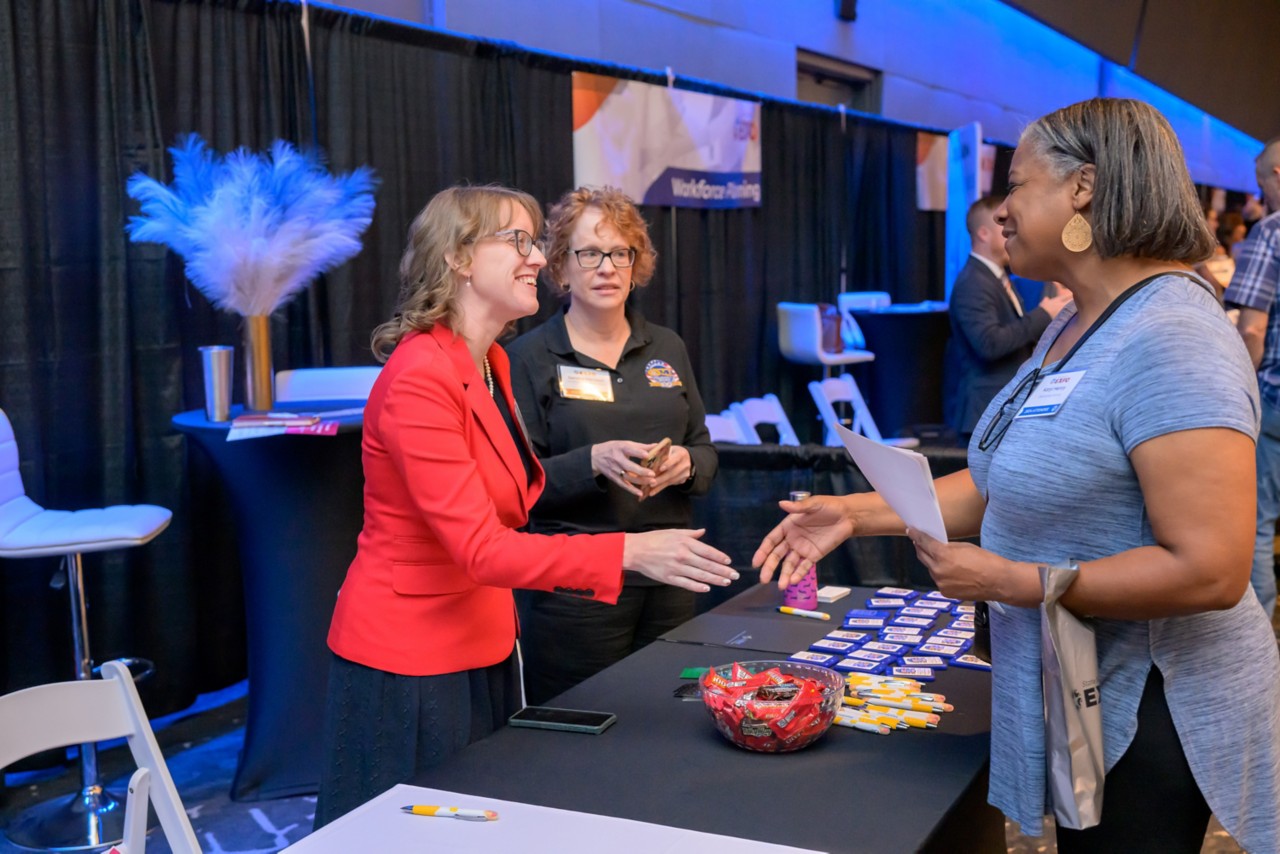 Two employees greeting an attendee at the Licensing and Regulation booth