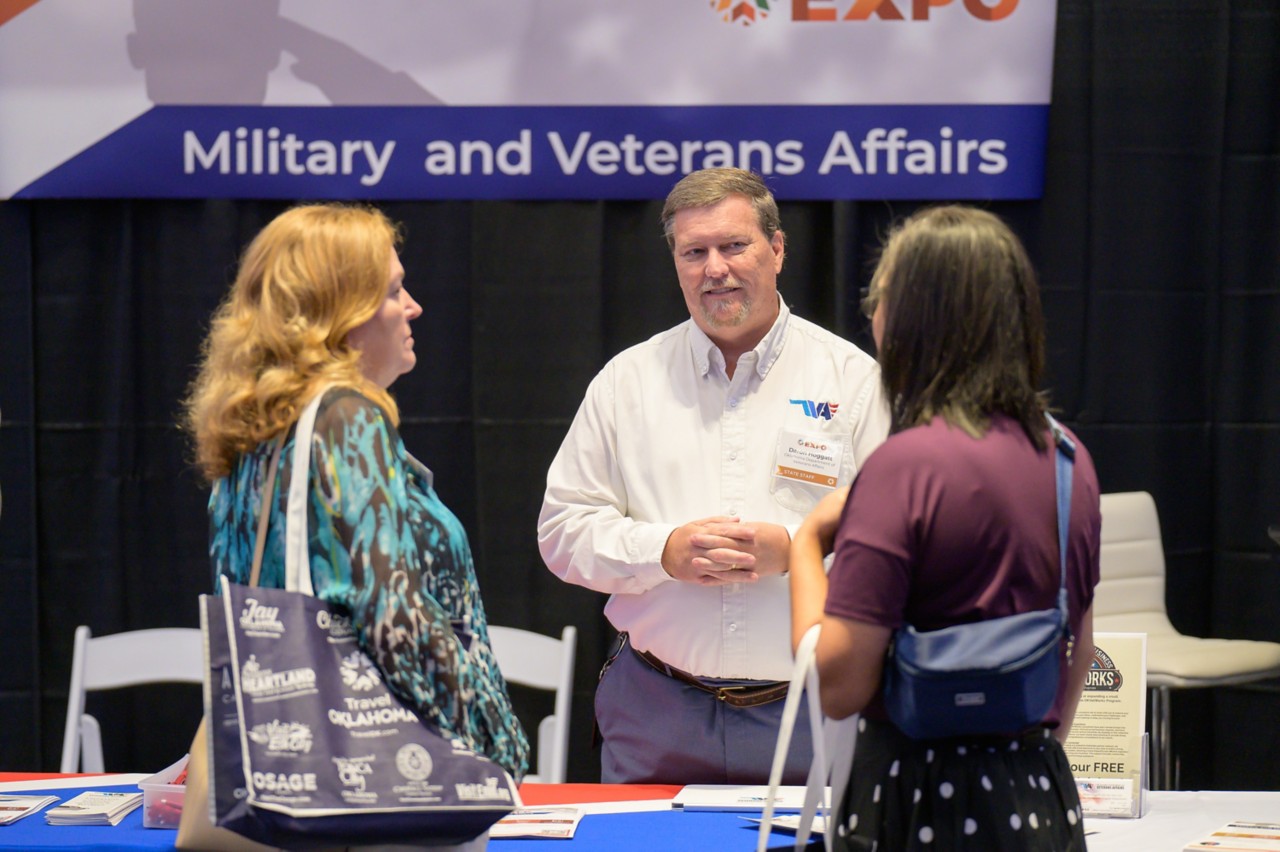 Two attendees engage with a state staff member at the Military and Veterans Affairs booth