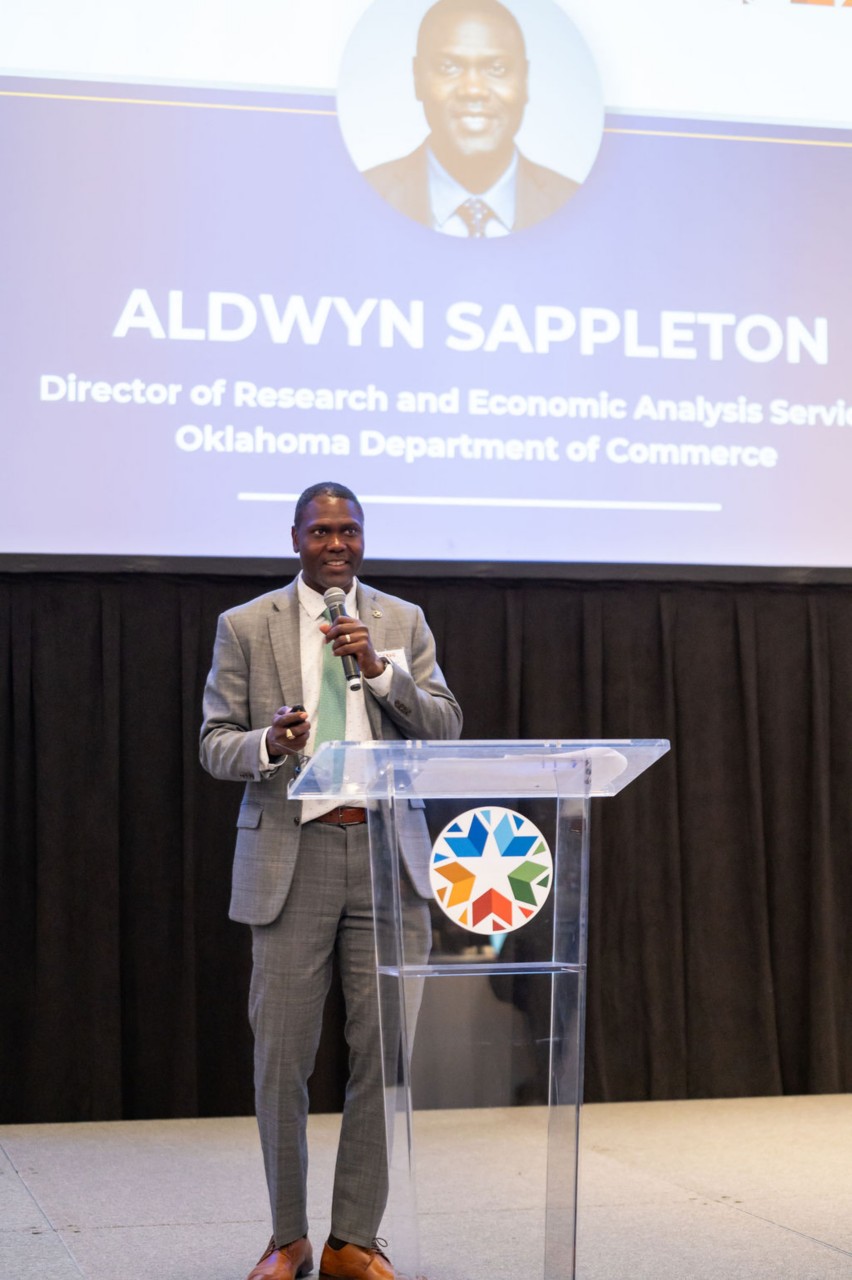 Midday speaker Aldwyn Sappleton at podium with projector screen