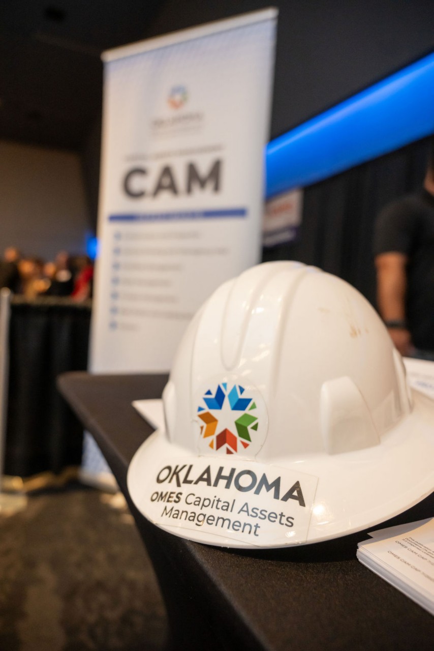 OMES Capital Assets Management-branded hard hard in front of a pop-up banner