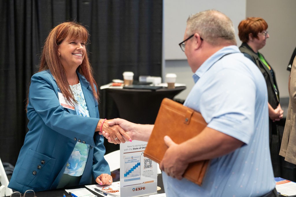 OMES Central Purchasing employee Darlene Saltzman shakes attendee's hand at the Statewide Contracts booth