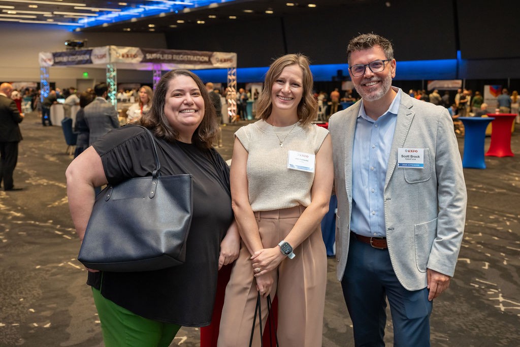 Three supplier attendees smile at front of ballroom