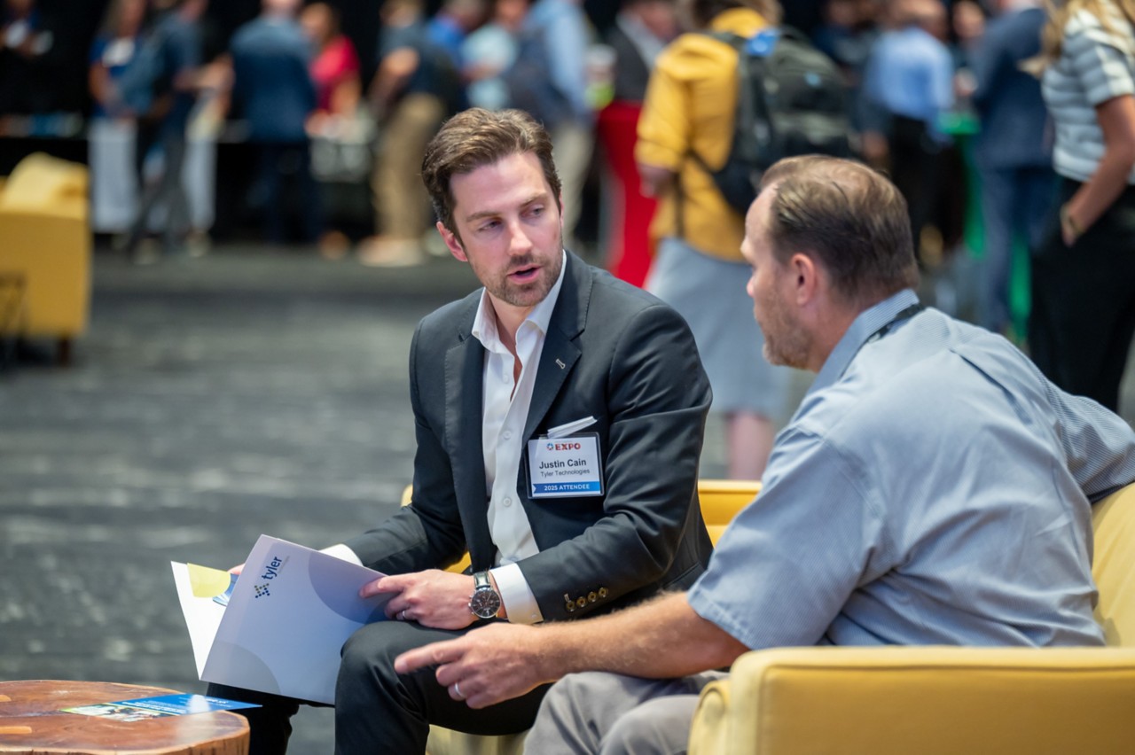 Two attendees sit and talk on yellow couch