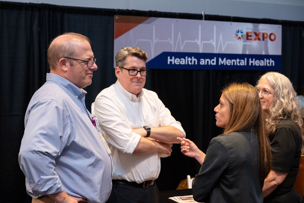 Two state staff talk with suppliers at Health and Mental Health booth