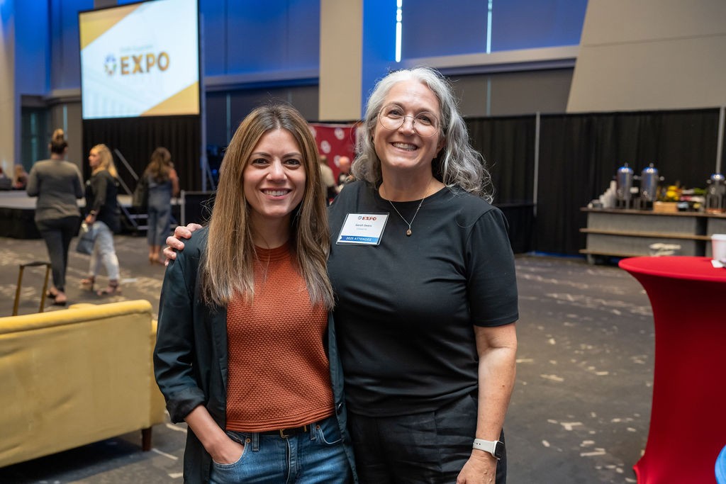 Two attendees smiling in front of ballroom speaker stage